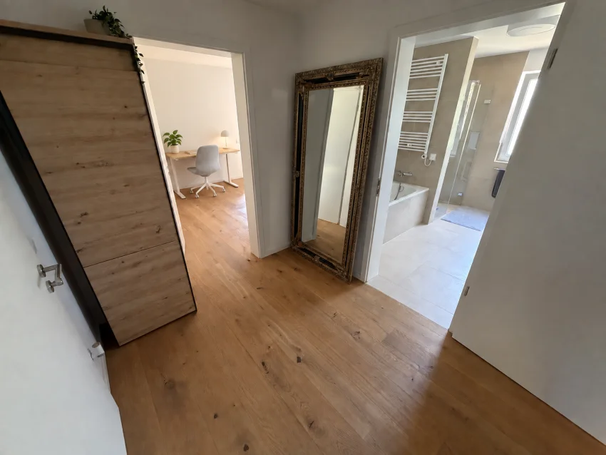 Entrée avec armoire et miroir, vue sur le bureau avec chaise gris clair et la salle de bains